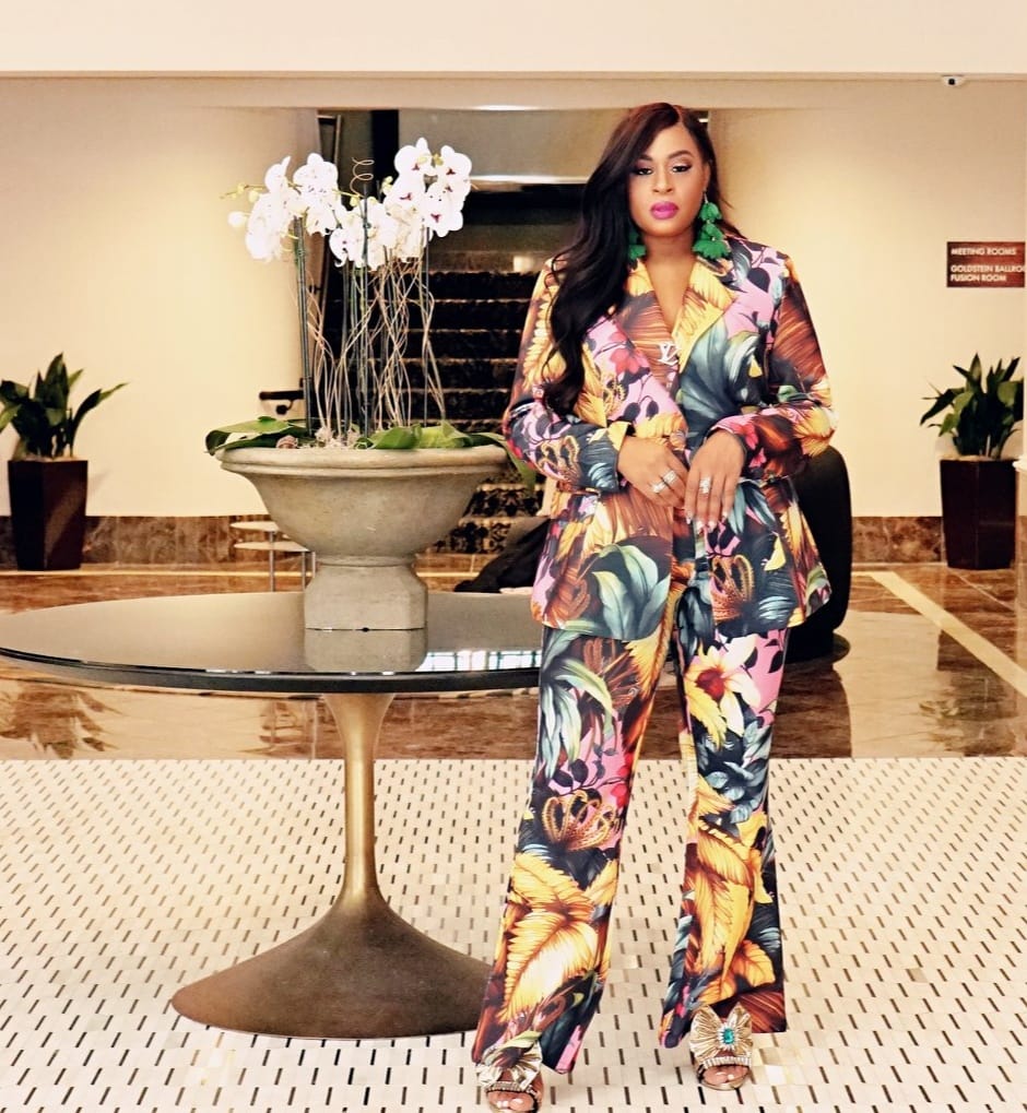 Jenni JCHIC Graham, founder of JCHIC LifeStyle®, wearing a vibrant tropical print suit in an upscale luxury setting, embodying professional style and elegance. The image showcases her brand's offerings of high-end branding, image consulting, and luxury lifestyle services